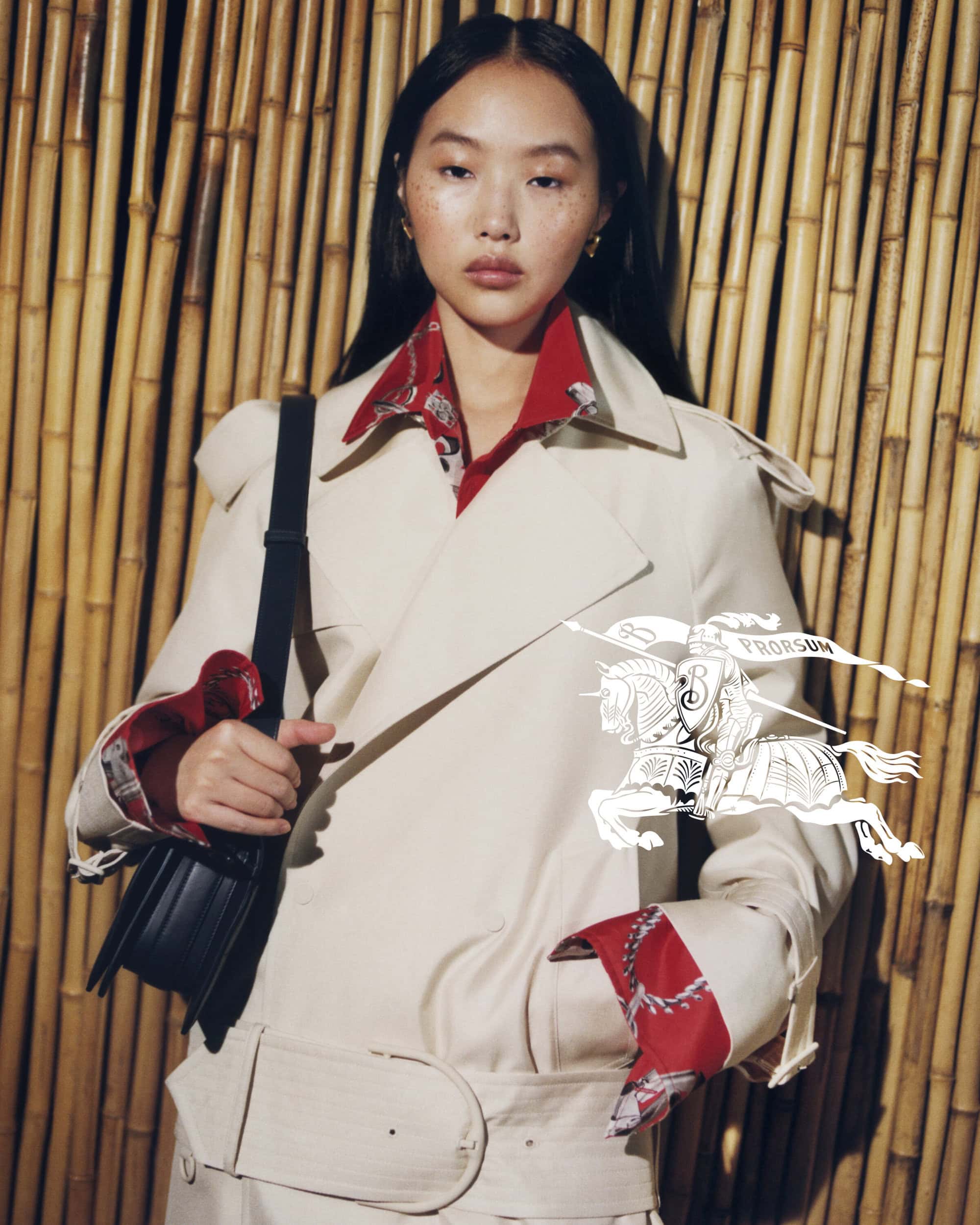 Asian woman in trench coat holding black purse against a bamboo background, graphic illustration overlay of equestrian knight logo.