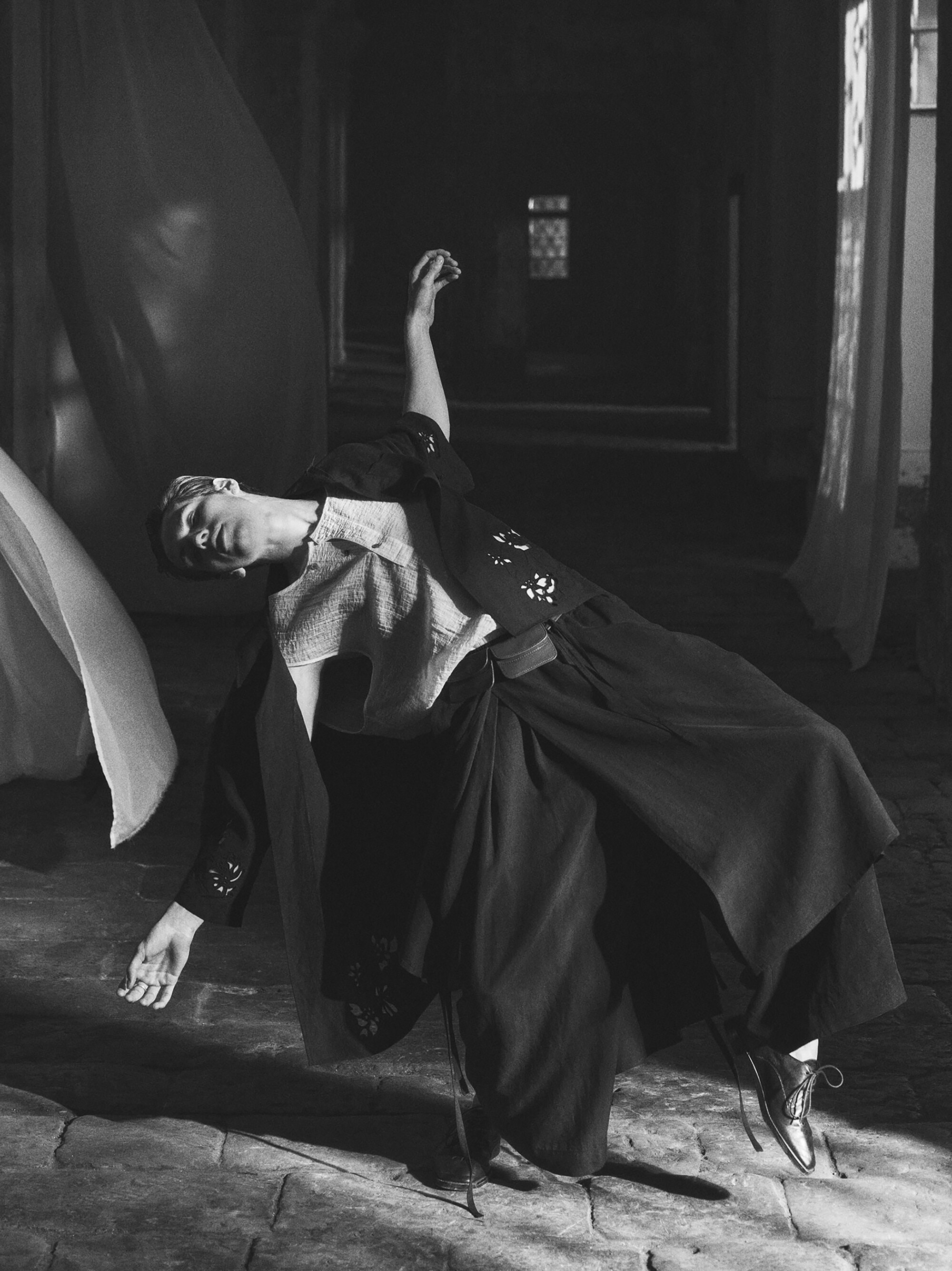 Dramatic black and white studio shot of a woman in motion, wearing flowing clothing, captured with artistic lighting and composition.
