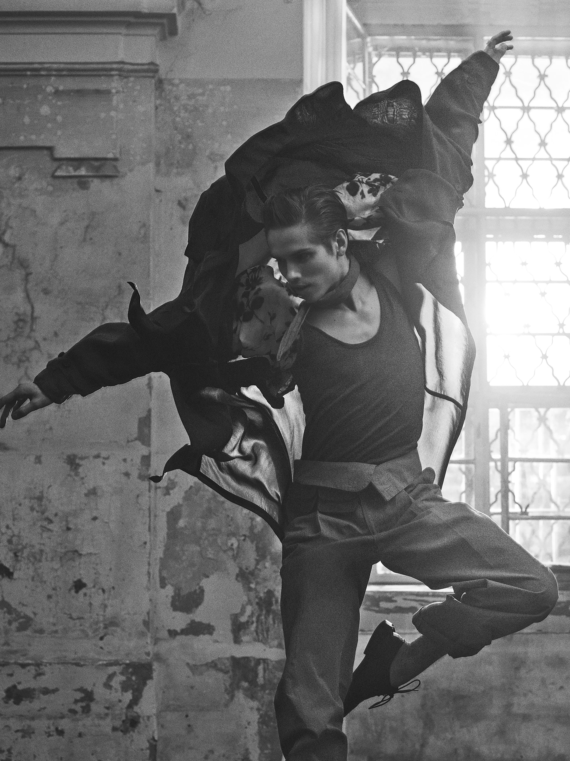 Monochrome fashion shot of two models in a dance pose. One is held up by the other who is wearing a tank top and pants.