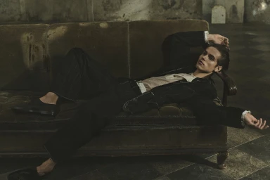 Male model lounging on an olive velvet sofa wearing a dark suit jacket and trousers for Zara Spring 2024 campaign