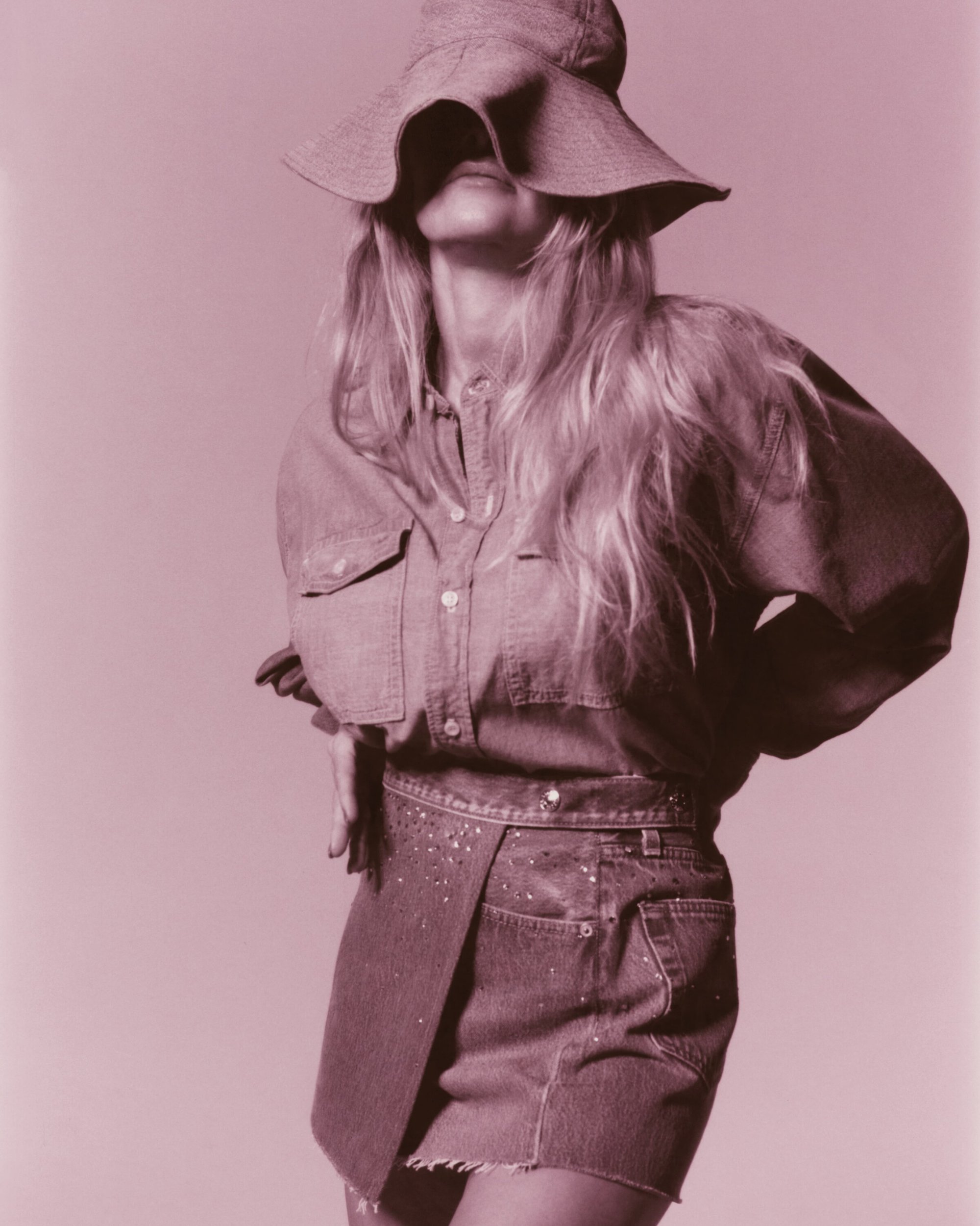 Woman in a denim outfit wearing a floppy bucket hat. The model has long blonde hair and wears a matching denim shirt and skirt.