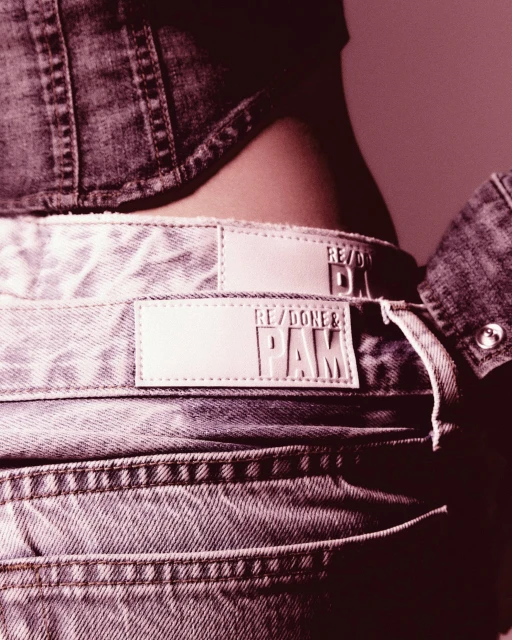 Close-up of a person wearing a denim jacket and light-wash jeans featuring brand label details; fashion, clothing, and style.