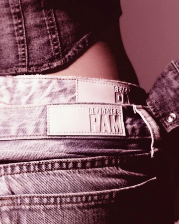Close-up of a person wearing a denim jacket and light-wash jeans featuring brand label details; fashion, clothing, and style.