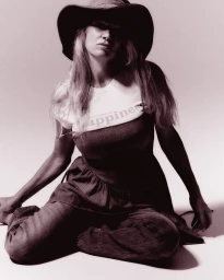 Woman wearing a wide-brimmed hat, graphic t-shirt, and denim apparel seated against a plain backdrop for RE/DONE.