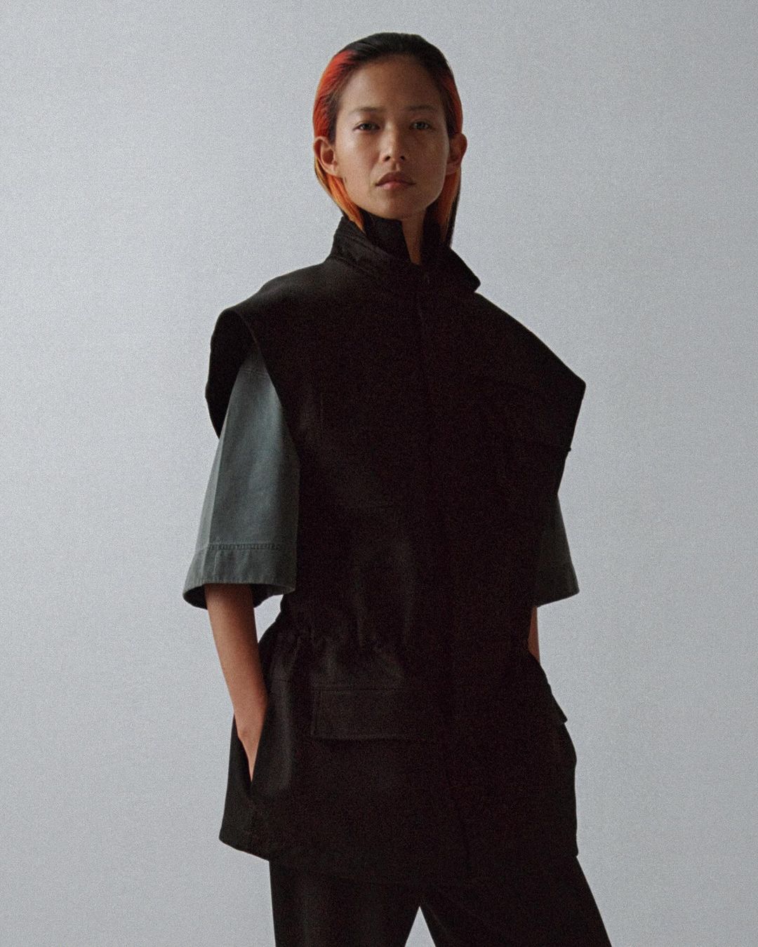 Stylish woman in a dark vest and pants, posing in a light studio. Fashionable clothing, soft light, and neutral background.