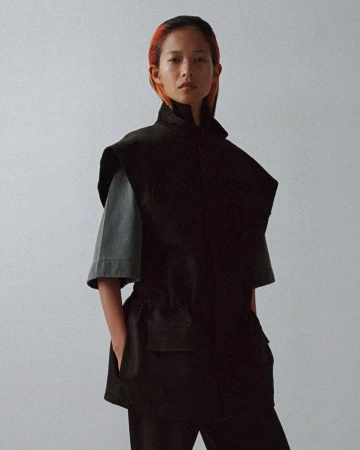 Model with dyed hair wearing a black vest and grey t-shirt against a grey studio backdrop for Phoebe Philo.