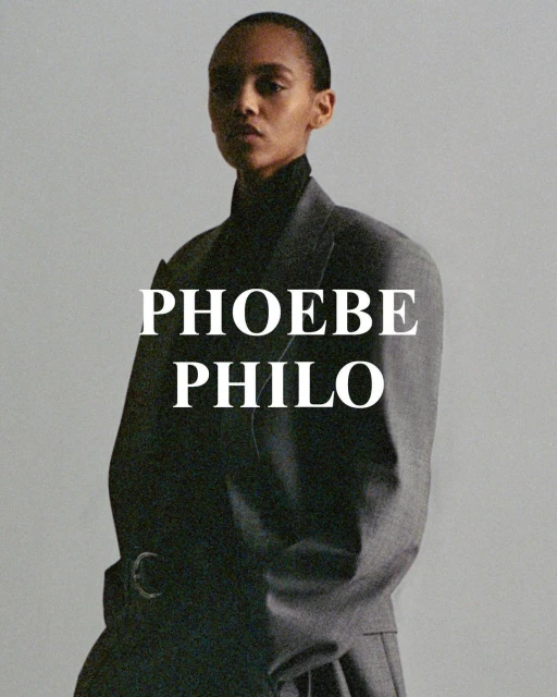 Fashion portrait of a woman wearing a grey jacket and black turtleneck against a neutral background with the text PHOEBE PHILO.