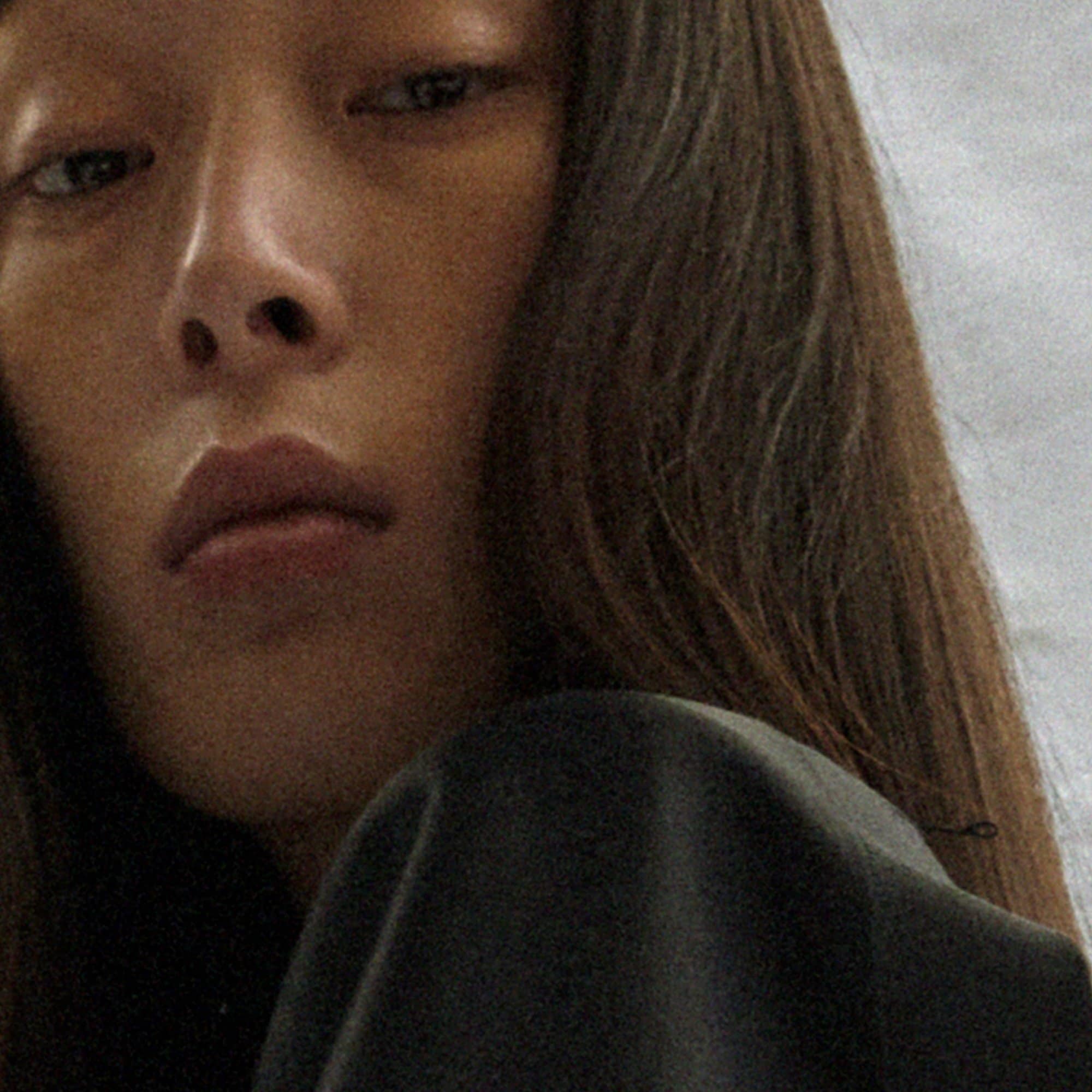 Close-up portrait of an Asian adult female with dark hair and dark eyes, wearing a dark top, set against a muted grey background.
