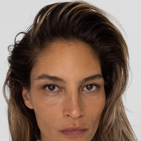Close up portrait of a woman with dark swept-back hair and natural makeup against a plain light background.