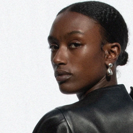 Close-up portrait of a Black woman wearing silver drop earrings against a white background for Phoebe Philo.