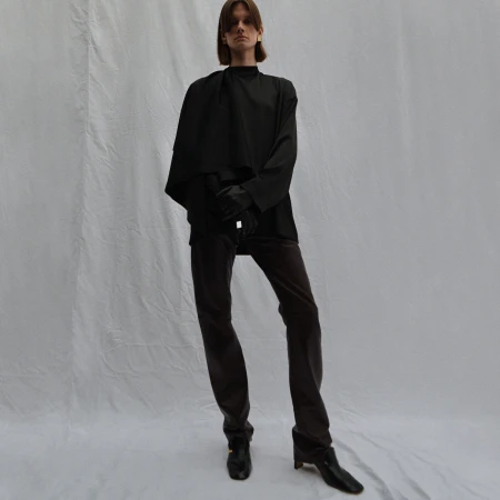 Model wearing a black top and dark trousers against a white seamless fabric backdrop
