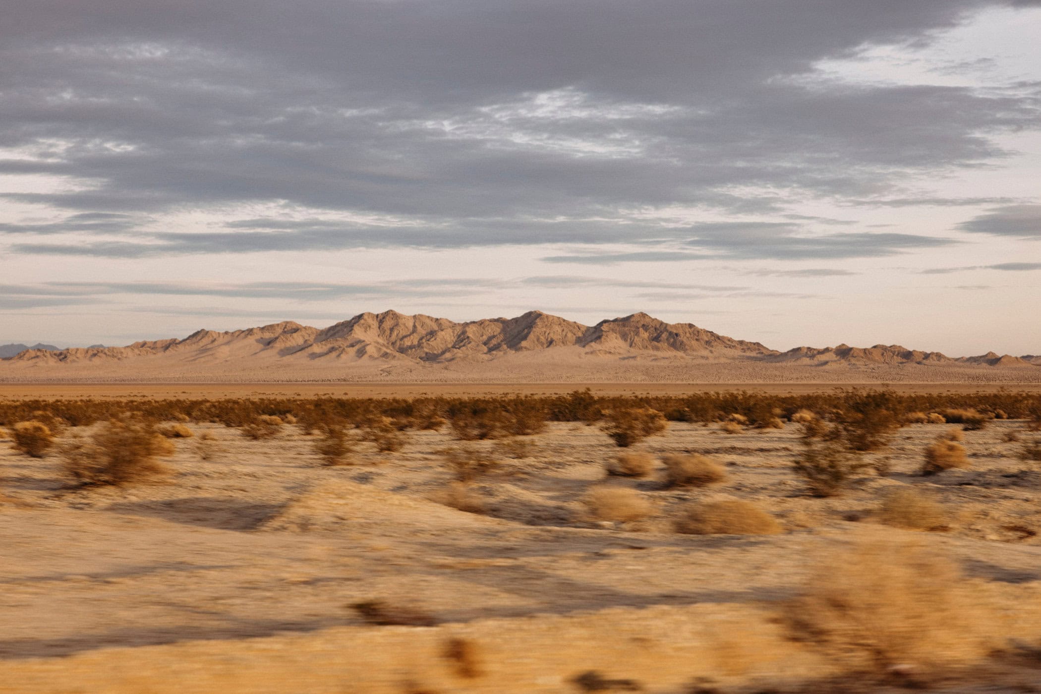 Arid desert landscape with distant mountains under a cloudy sky, showcasing natural beauty and a remote, scenic environment.