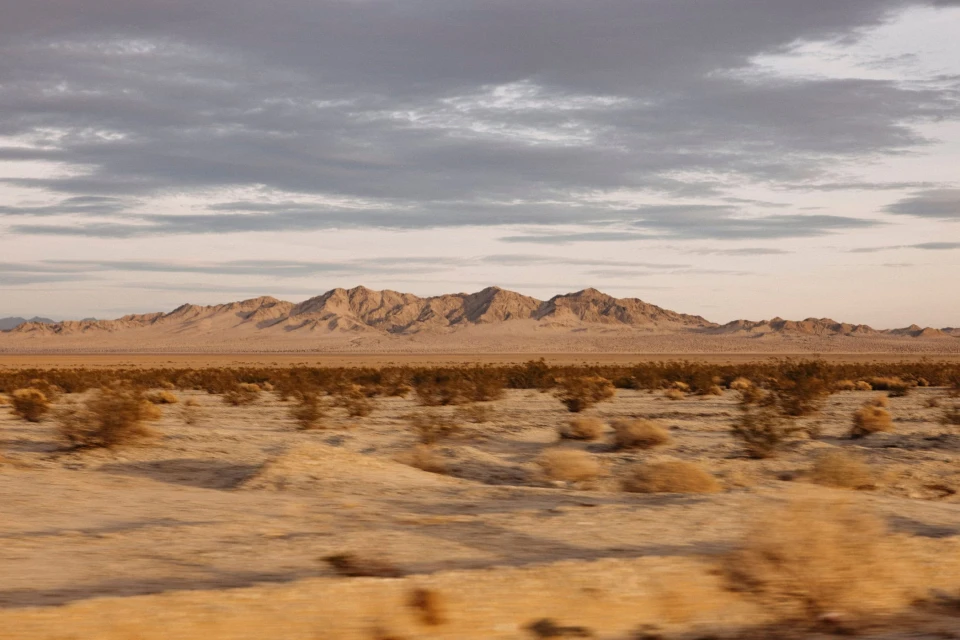 Arid desert landscape with distant mountains under a cloudy sky, showcasing natural beauty and a remote, scenic environment.
