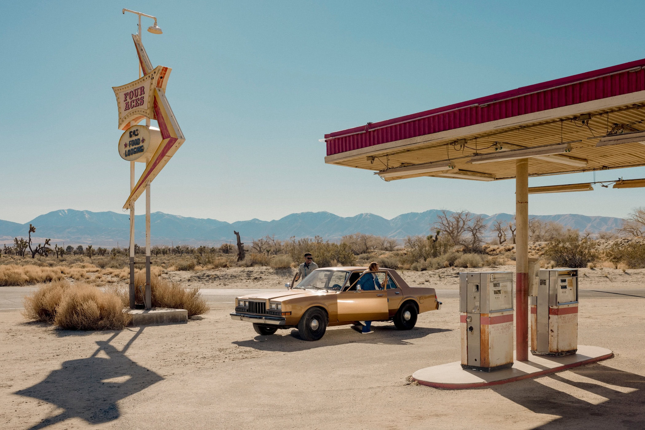 Vintage service station in a desert landscape with a gold sedan, gas pumps, and a retro star sign under a clear blue sky
