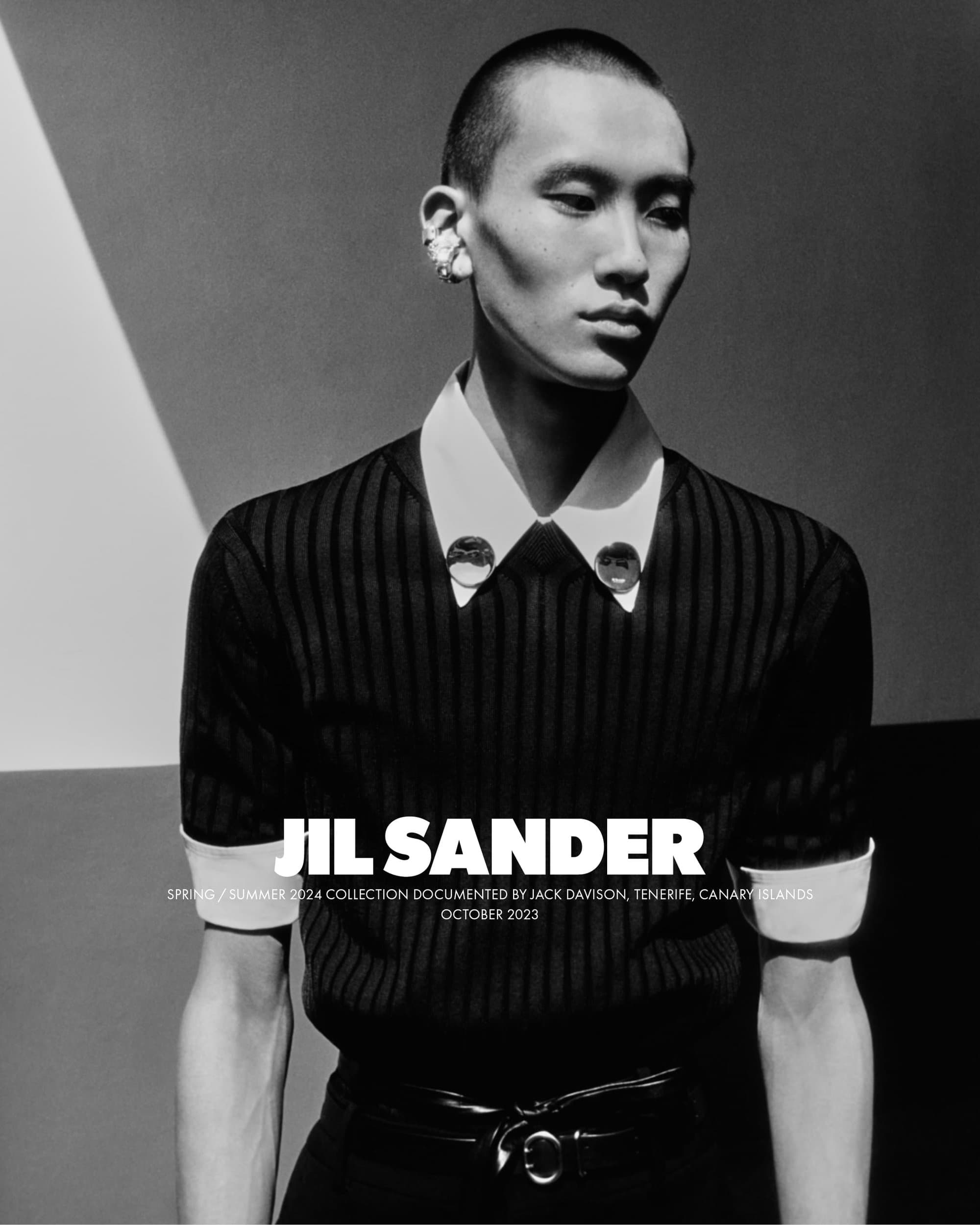 Monochrome studio shot of a young adult male model with short hair, wearing a collared shirt and tie, against a geometric background.
