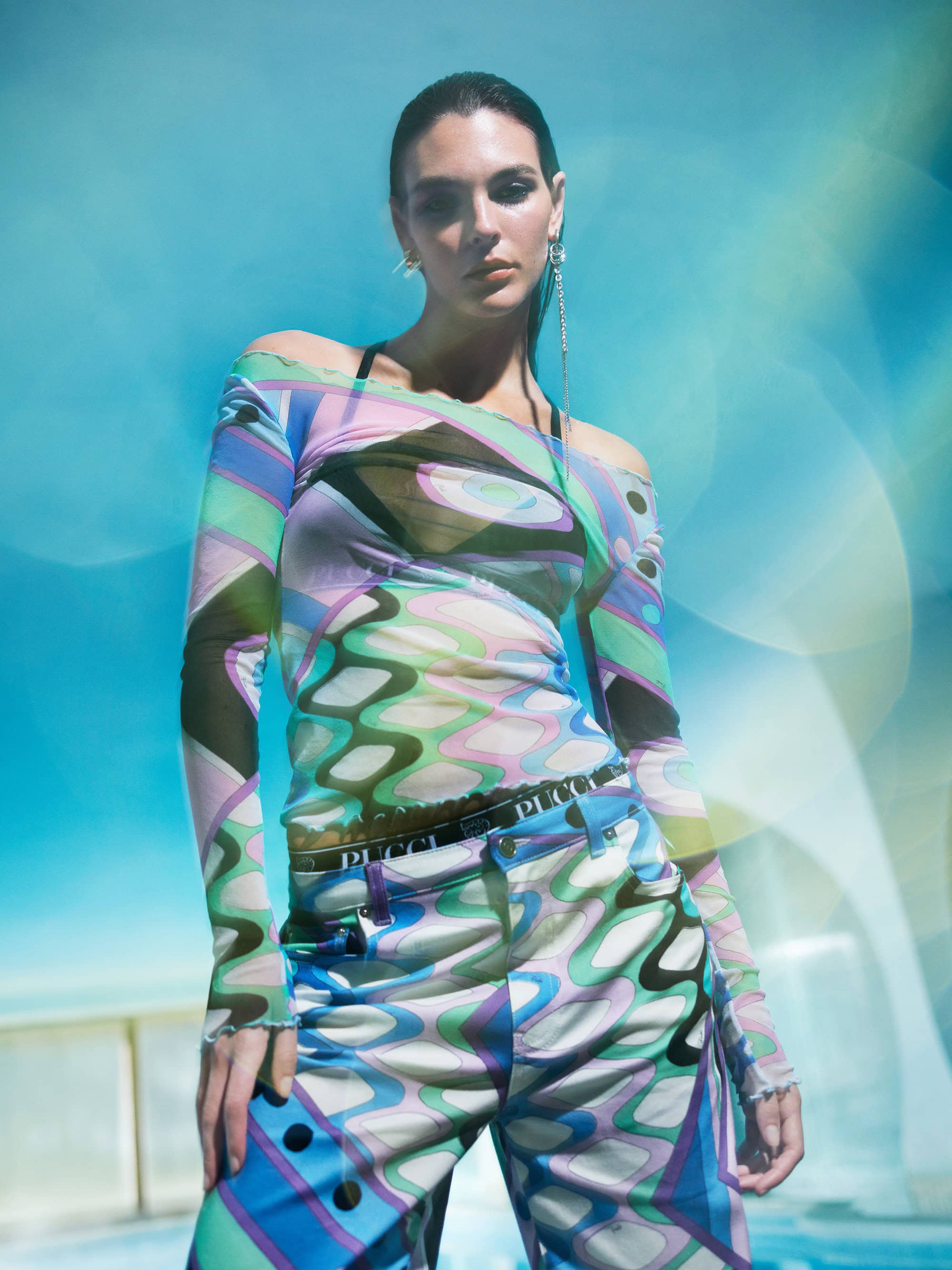 Woman in printed top and pants poses against an aqua background. She has long dark hair, wears earrings, and a PUCCI branded waistband.