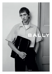 Man wearing a light short-sleeve button-down shirt holding a black briefcase in an indoor setting for Bally Spring 2024 campaign