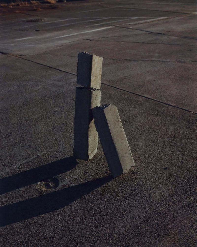 Concrete blocks stacked outdoors on a flat asphalt surface with visible shadows under natural lighting conditions, creating simple art.