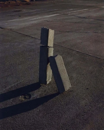 Concrete blocks stacked outdoors on a flat asphalt surface with visible shadows under natural lighting conditions, creating simple art.