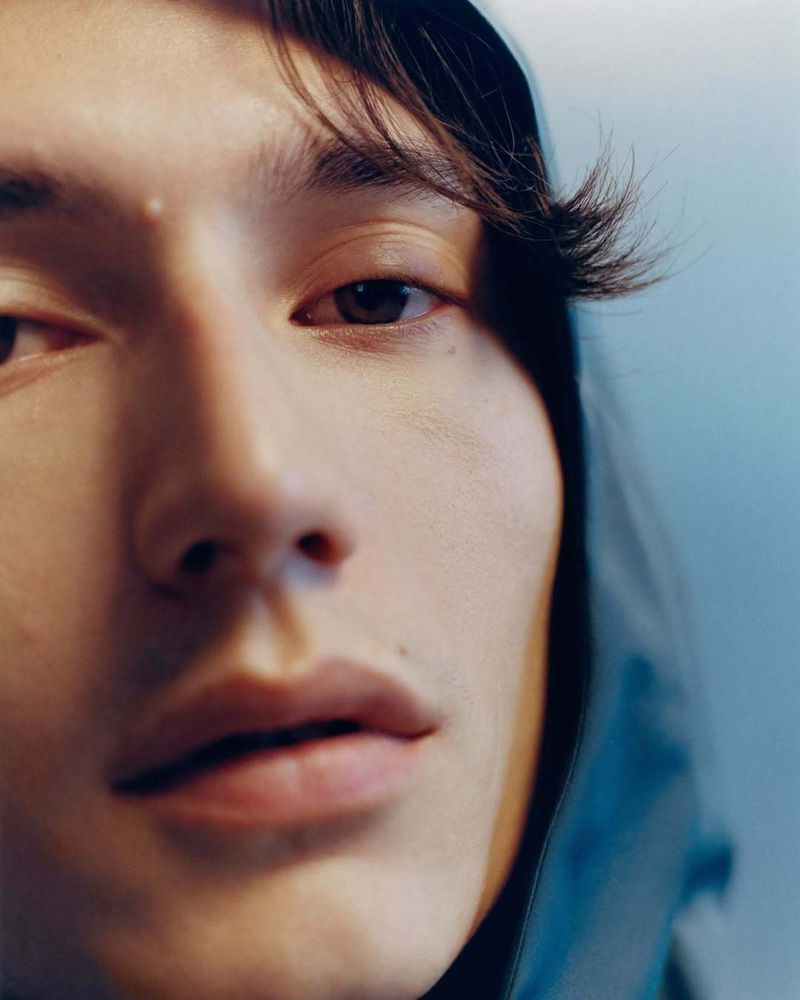 Close-up portrait of an adult with dark hair and eyes against a soft blue background, showcasing skin texture and details of facial features.