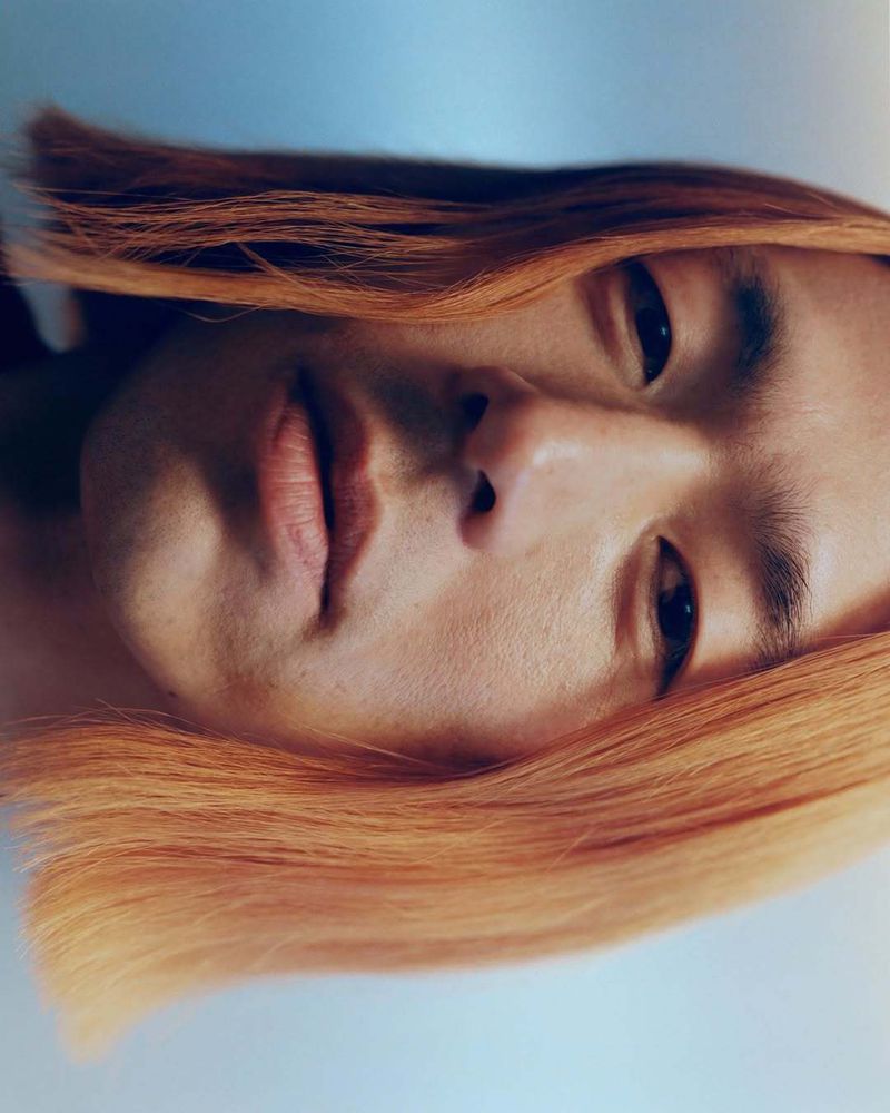 Close-up portrait of a person with peach-colored hair looking directly at the camera. The soft, diffused lighting creates a serene mood.
