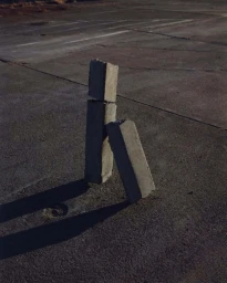 Three stacked concrete blocks on a weathered asphalt surface casting long shadows under natural light.