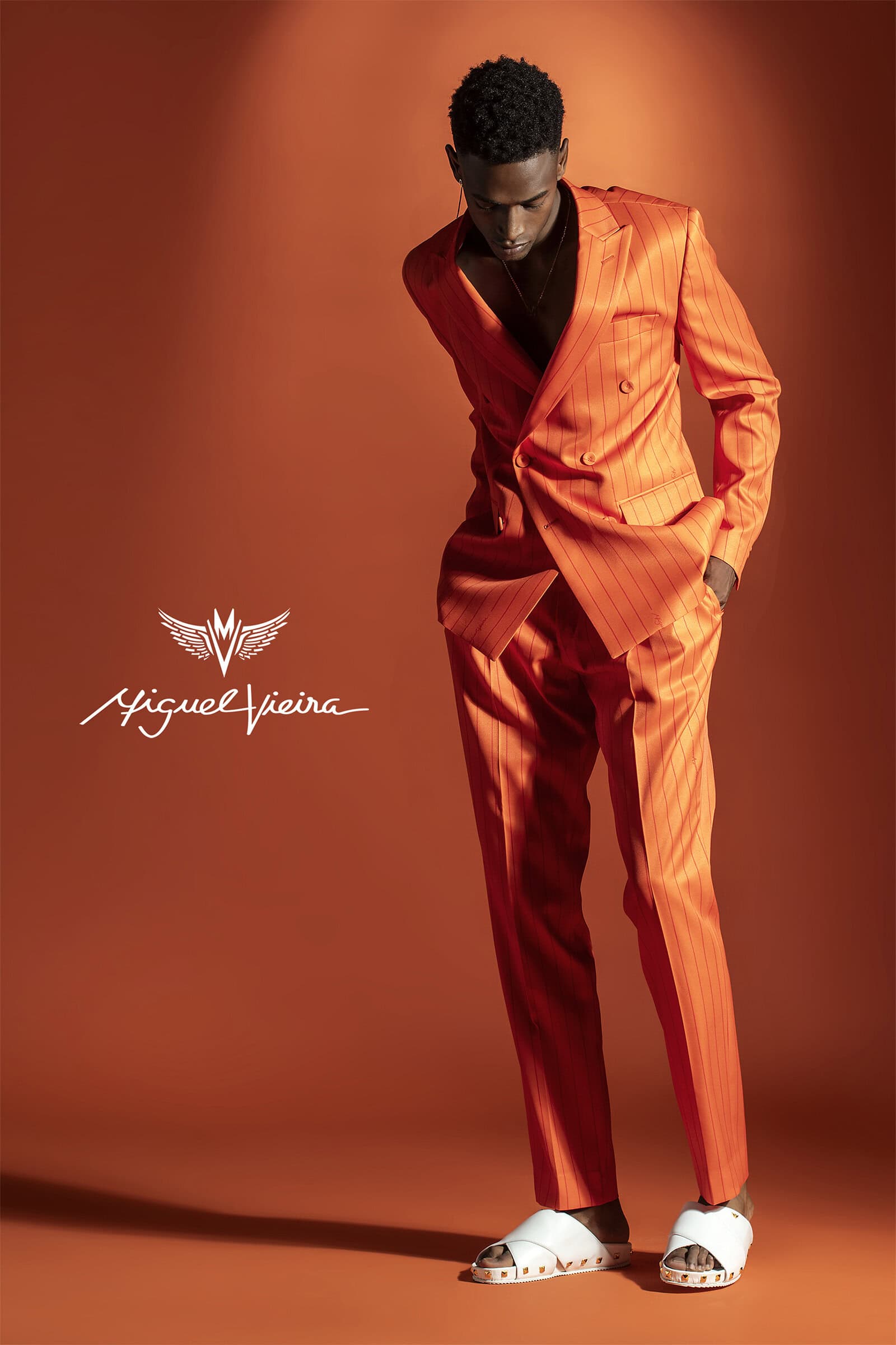 A Black male fashion model in a bright orange striped suit poses in a studio setting, creating a bold and stylish visual statement.