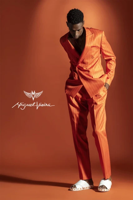 A Black male fashion model in a bright orange striped suit poses in a studio setting, creating a bold and stylish visual statement.