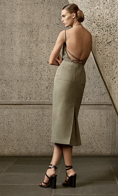 Back view of a woman in a midi dress with spaghetti straps and strappy heels, posing against a textured gray wall.