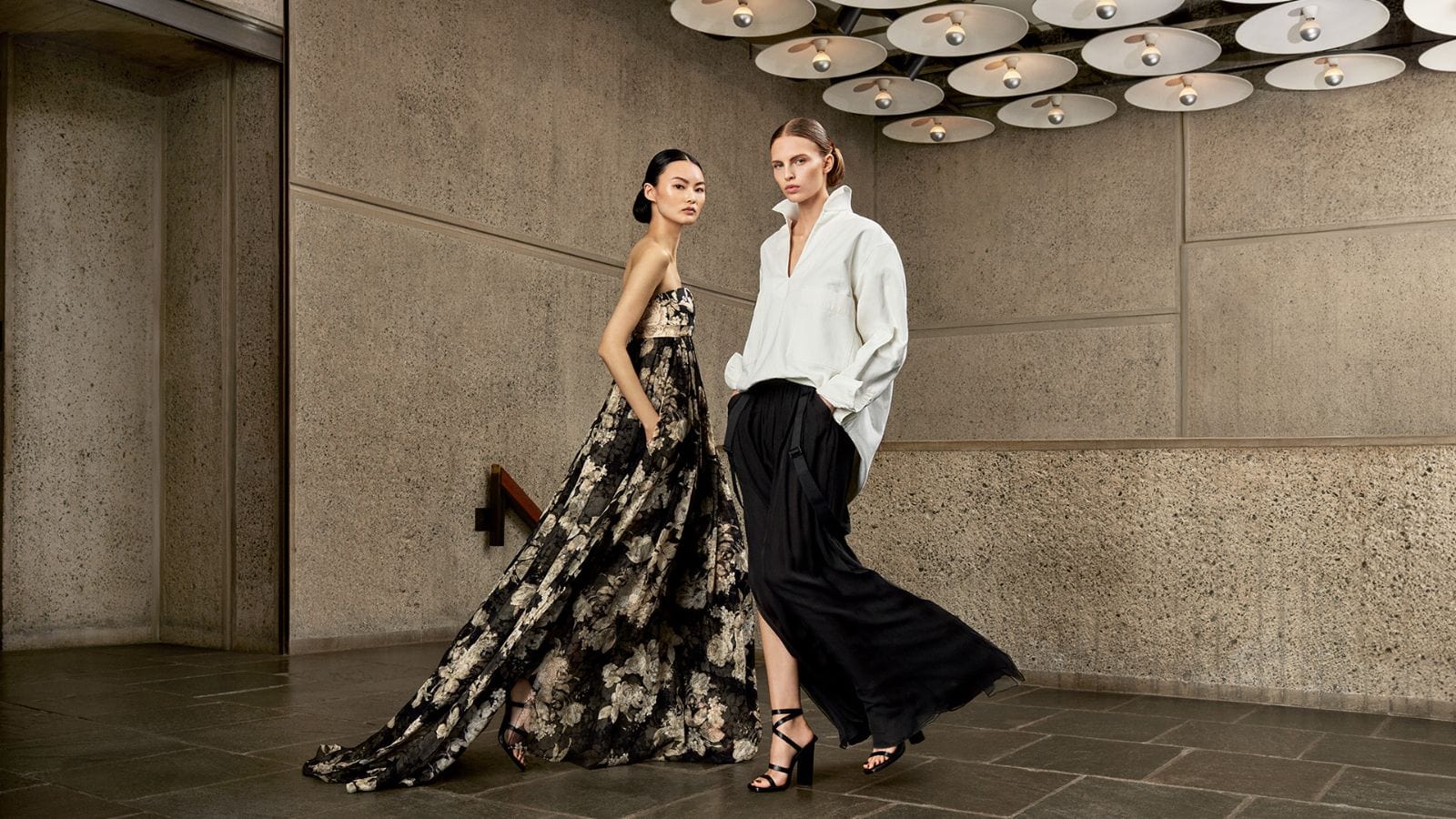 Two female models posing in architectural interior with concrete walls and modern saucer ceiling lights for Max Mara spring 2024 campaign