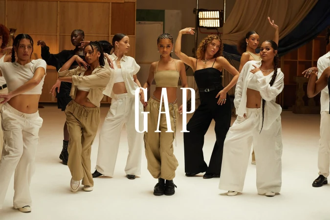 Group of young adult models wearing casual, neutral-toned Gap clothing perform a dance routine in a bright studio setting. 