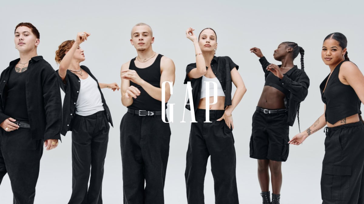Group of six diverse individuals in black outfits posing in a brightly lit studio setting for a GAP fashion campaign. 