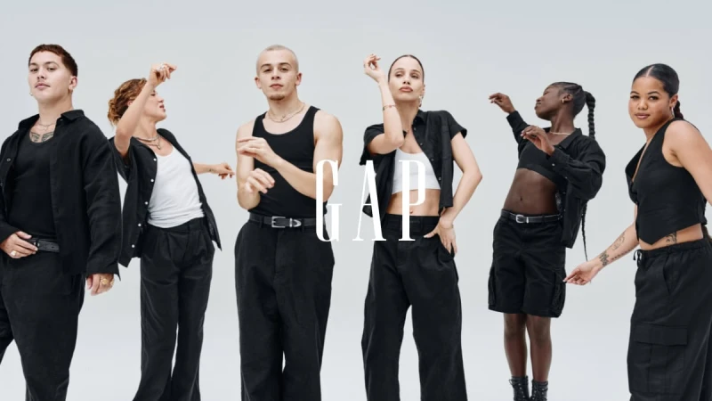 Group of six diverse individuals in black outfits posing in a brightly lit studio setting for a GAP fashion campaign. 