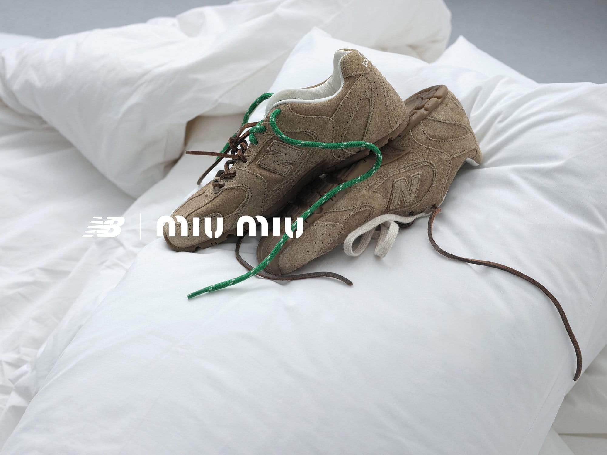 Two tan New Balance sneakers with brown and green laces are displayed on a white pillow, with the Miu Miu brand logo visible.
