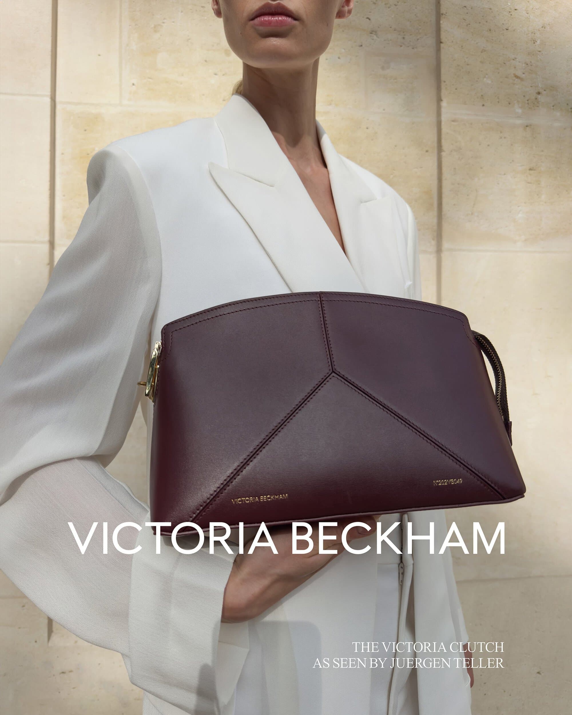 Close-up of a stylish burgundy clutch with geometric design, presented by a fair-skinned model in a white suit against a neutral background.