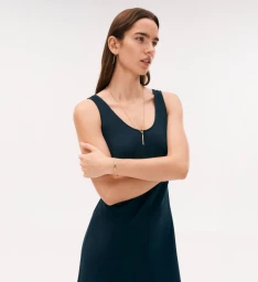 Model in a dark blue sleeveless dress wearing a gold pendant necklace against a plain white background