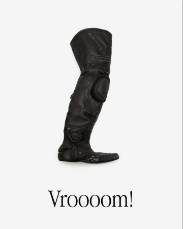 Elevated studio shot of a tall black leather motorcycle boot with protective pads against a white background with 'Vroooom!' text below.
