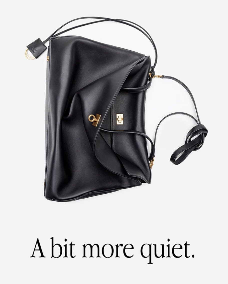 Studio shot of a black leather handbag with gold hardware, draped against a white background with the phrase 'A bit more quiet.'