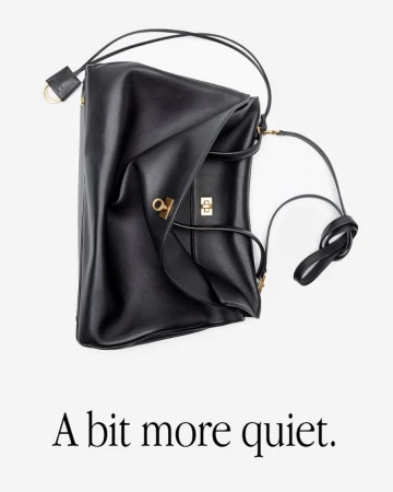 Studio shot of a black leather handbag with gold hardware, draped against a white background with the phrase 'A bit more quiet.'