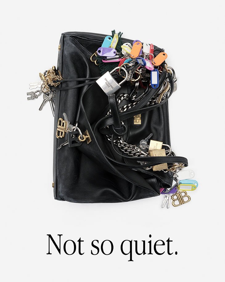 Black Balenciaga handbag covered in keys and keychains, photographed in a studio setting against a white backdrop.