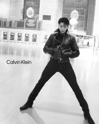 Jung Kook wearing a black leather jacket and trousers posing inside Grand Central Terminal for Calvin Klein