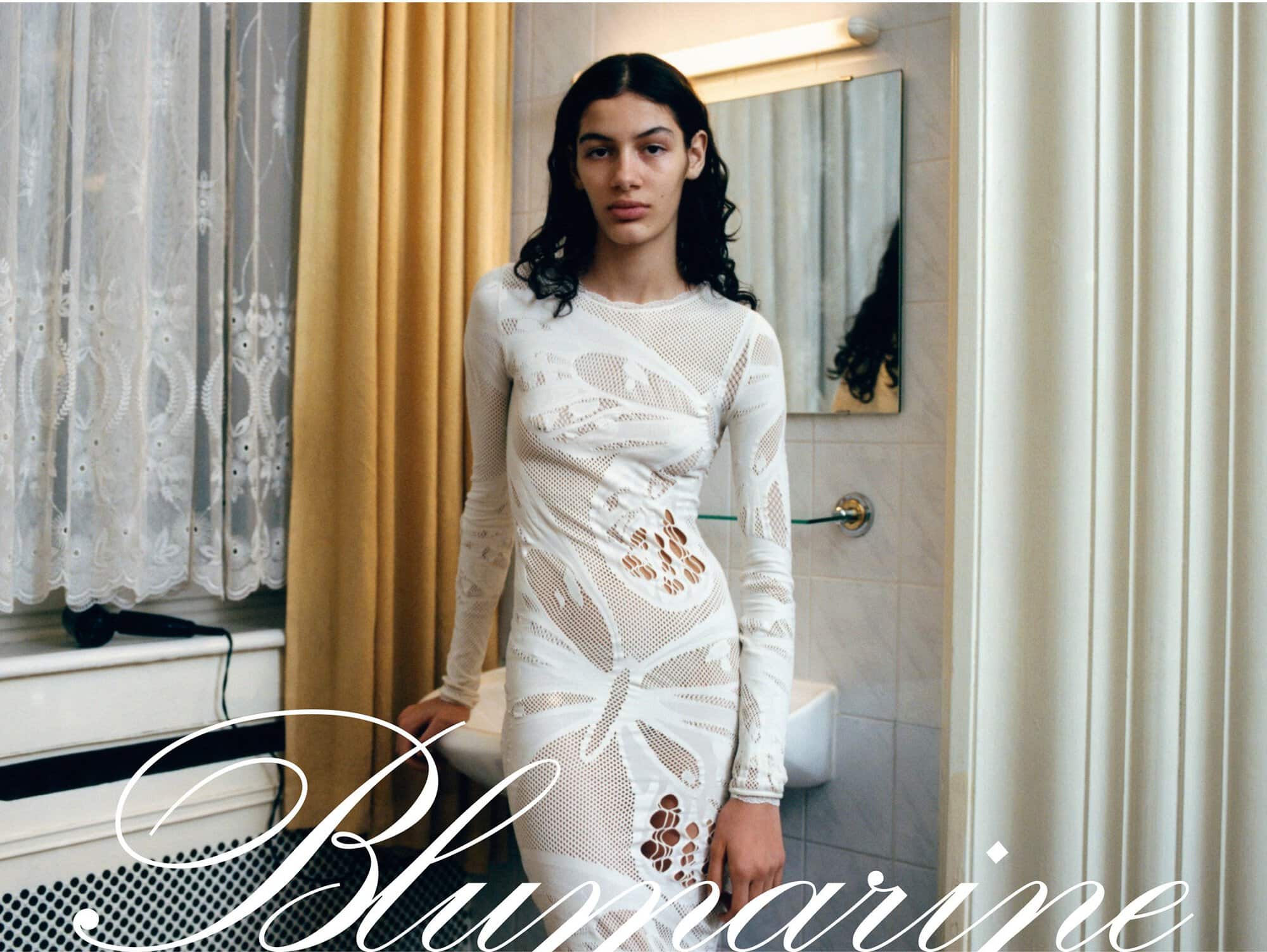 A fashion shot features a slender woman in a long white dress with cut-out details, posed against a bathroom backdrop with curtains and fixtures.