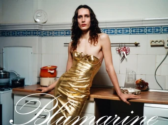 Model in a metallic gold strapless dress leaning against a kitchen counter for the Blumarine spring 2024 campaign.