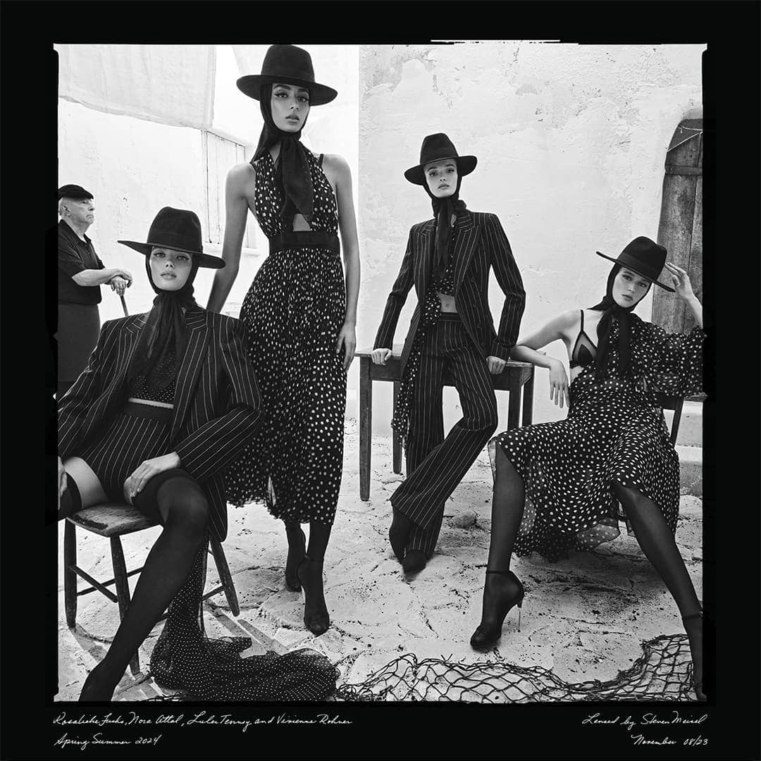 Black and white fashion editorial with four women models in patterned dresses and suits, wearing hats, set against a textured wall.