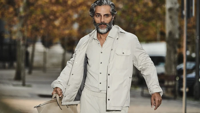 Joaquín Furriel walking outdoors wearing a beige jacket and holding a bag for Moncler Spring 2024 campaign