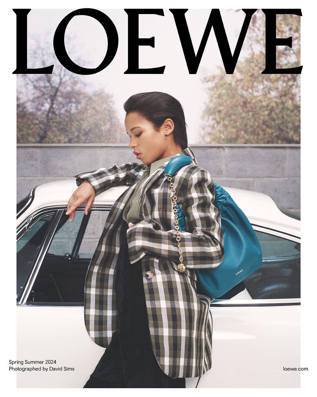 Fashion editorial featuring a woman in a blazer leaning against a vintage white car with a teal bag, and the LOEWE logo.