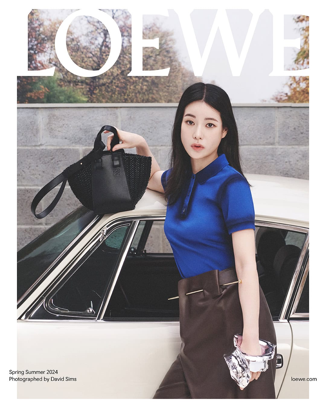 Fashion magazine cover featuring a young woman in a blue polo shirt and brown skirt next to a vintage car, holding a black bag.