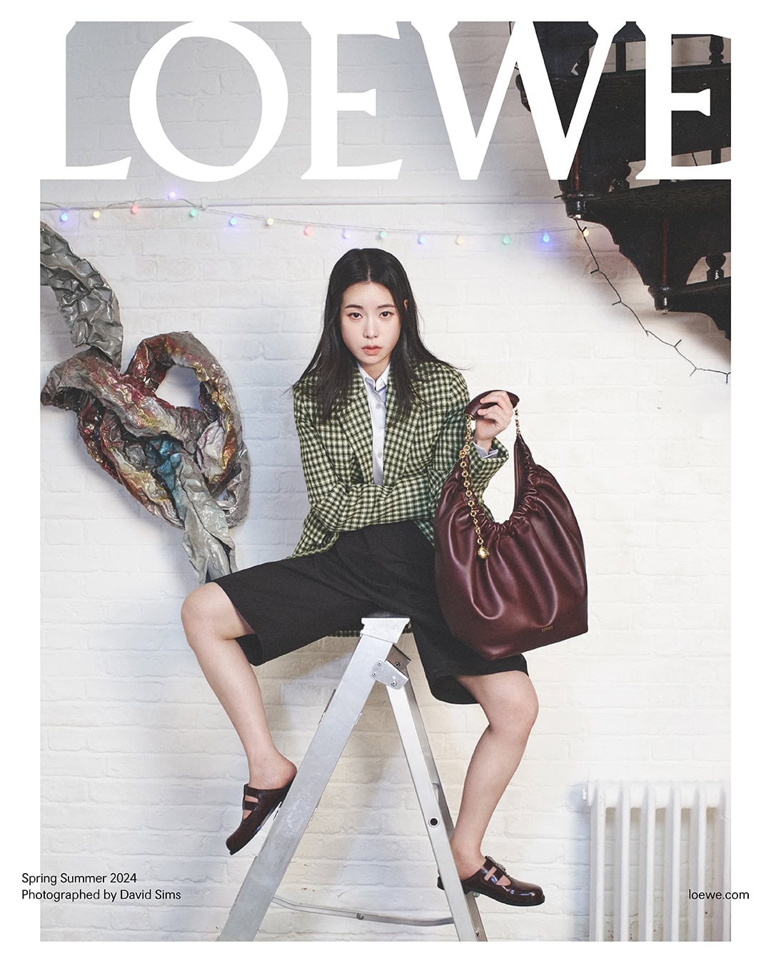 Magazine cover featuring a young woman seated on a ladder with a burgundy bag, wearing a green plaid blazer and dark shorts.