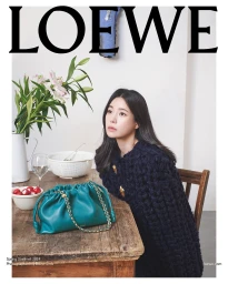 Lim Ji-Yeon seated at a wooden table next to a teal leather handbag for the Loewe Spring 2024 campaign, photographed by David Sims.