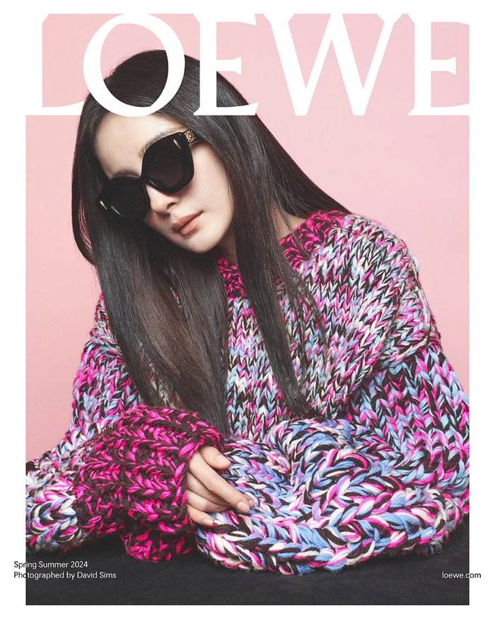 Woman wearing oversized sunglasses and a textured pink and blue knit sweater against a pink backdrop